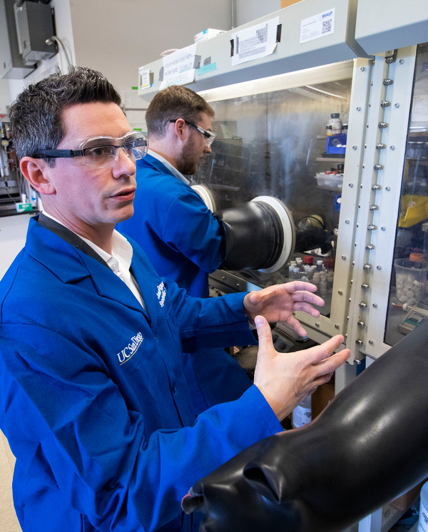 Professor Joshua Figuroa (lower left) describes the experiment he and Myles Drance successfully completed. Drance works in the glovebox in the background. Photo by Michelle Fredricks, UC San Diego Physical Sciences