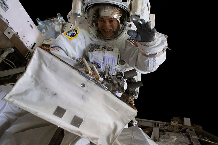 An astronaut smiles and waves at the camera while conducting a spacewalk