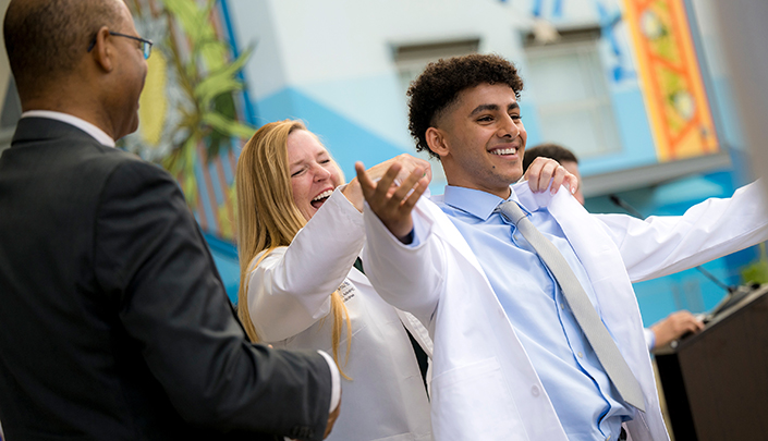 Dr. Michelle Daniel places a white coat on a new medical student during the ceremony. 