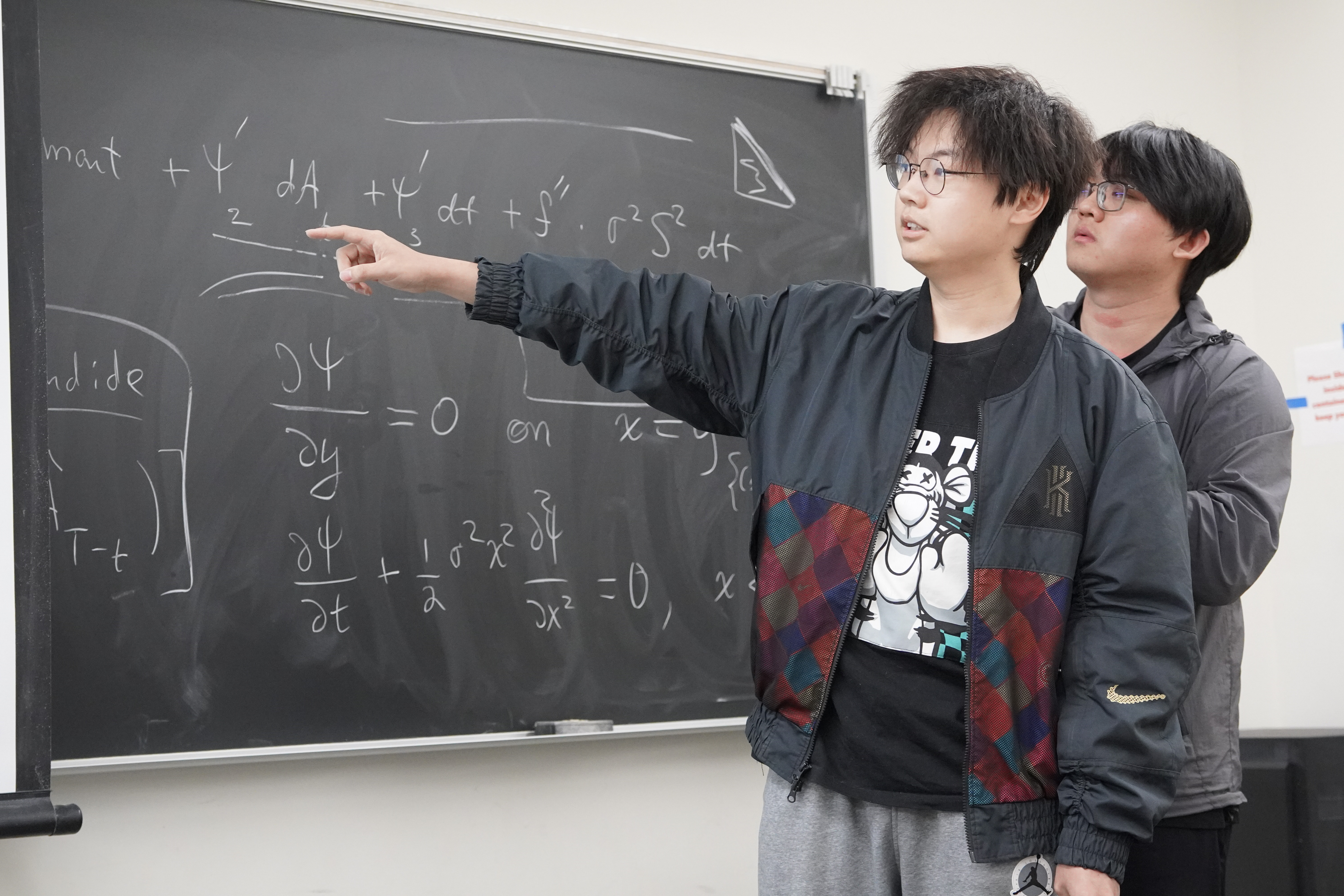 Two students talking about their findings written on a chalkboard