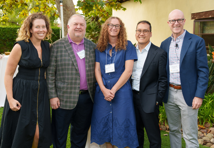 Group photo including two females and three males standing in a line facing the camera smiling. 