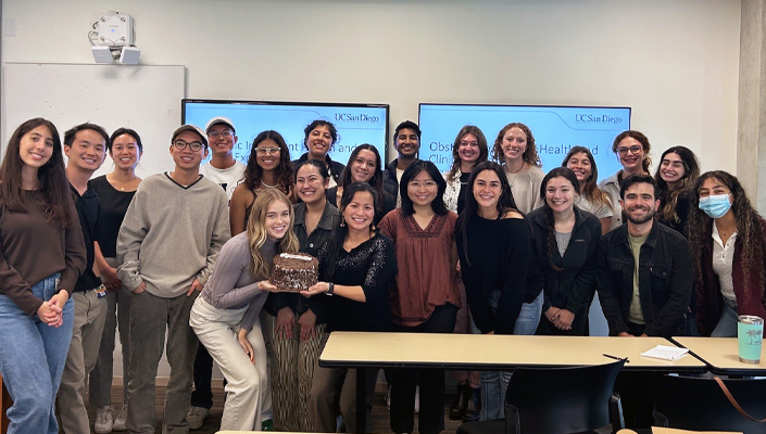 Class group photo of students and faculty member holding a cake and smiling towards the camera. 