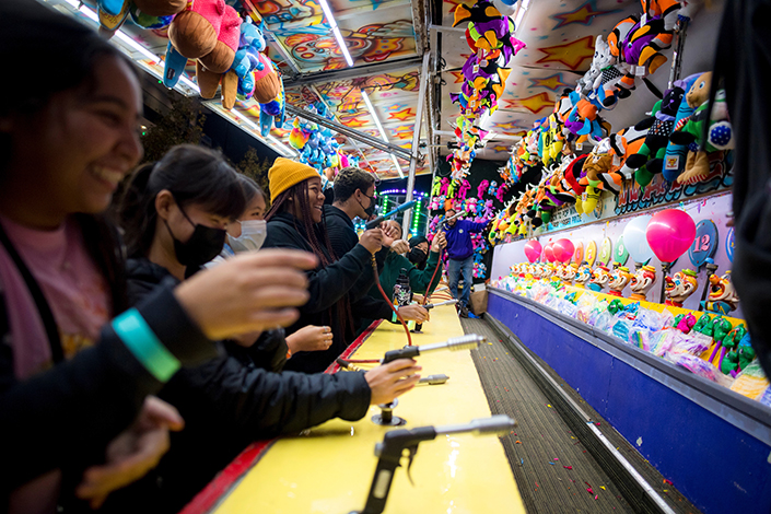 Students playing a carnival game, holding water guns and shooting the spray to blow up a balloon until is pops.