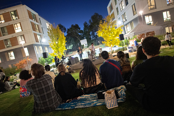 A group of students sitting on blankets in the grass listening to live music.