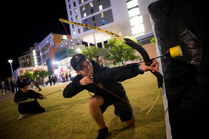 A student holds a bow with a fake arrow and hides behind an inflatable barrier during a game of archery tag.