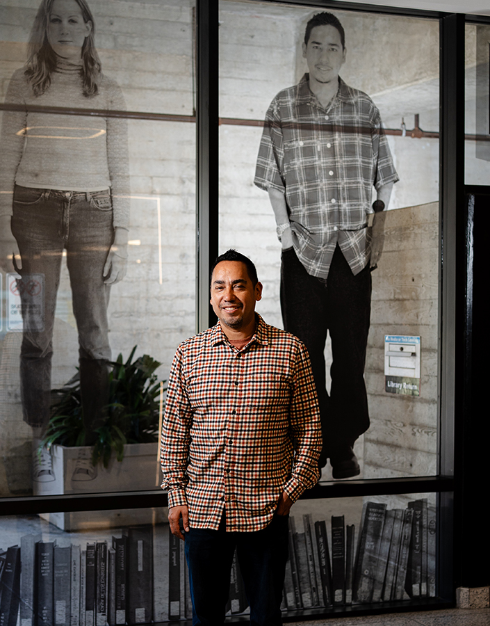 A person stands in front of a glass image of a two college-aged students.