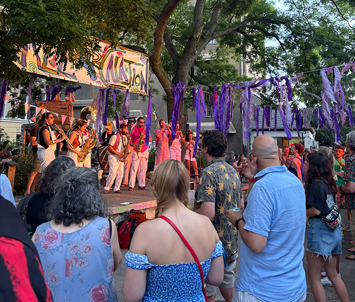 A colorful street parade with musicians performing on stage and a crowd watching.