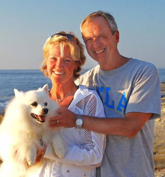 photo of man and woman at the beach, holding a dog