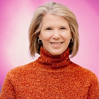 Woman with blonde hair in orange sweater smiling against a pink background