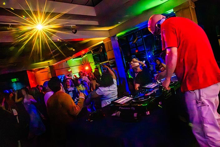 A DJ spins records as people dance in the background.