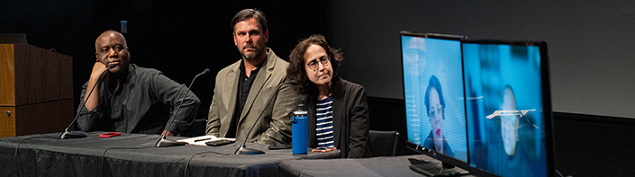 Three people and two screens on stage