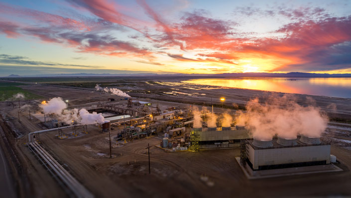 The sun sets, shining light across a large body of water and a geothermal plant generating clean energy.