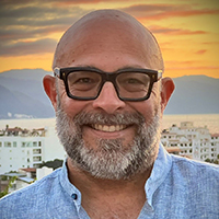 Headshot of man with glasses and a beard in front of a sunset