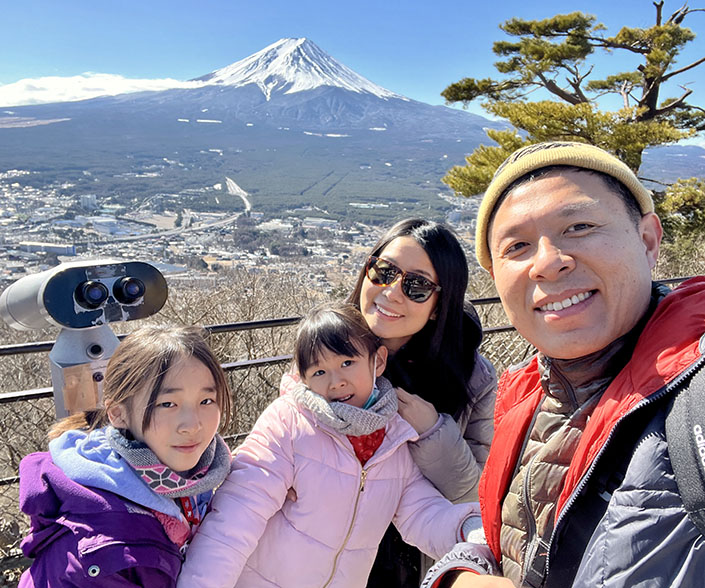 The Choi family smiles for a photo with a mountain and tree in background.