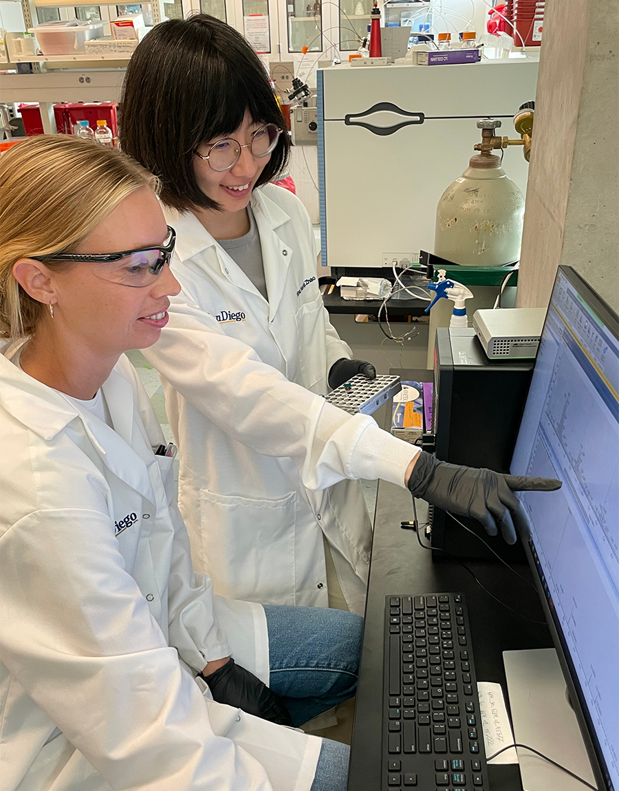 Two female researchers in white lab coats examining date on computer