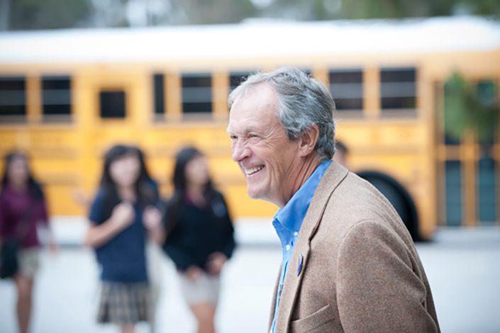Man looking off camera with a smile with school bus and students in the background
