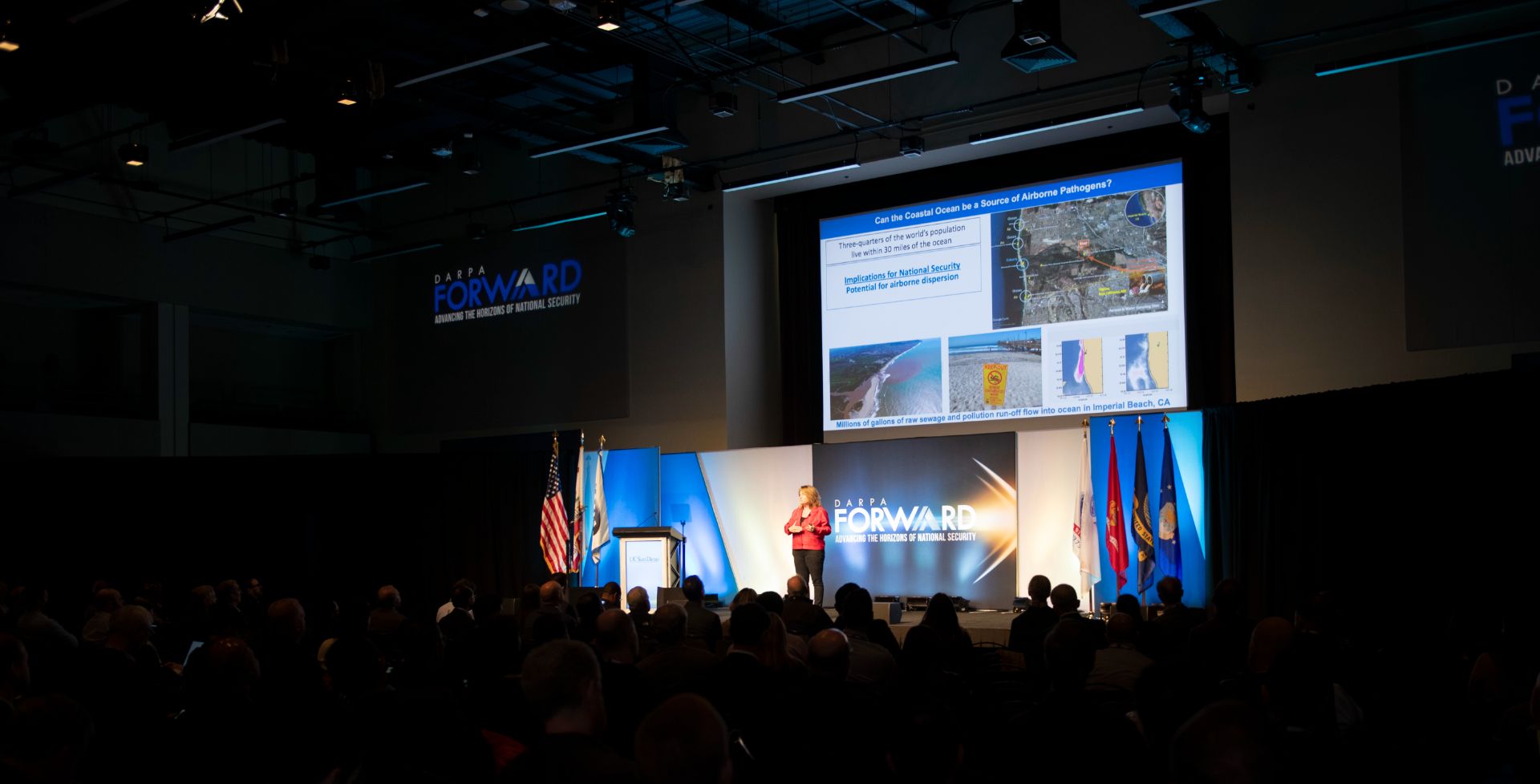 Kim Prather stands at the front of an auditorium beneath a projection.