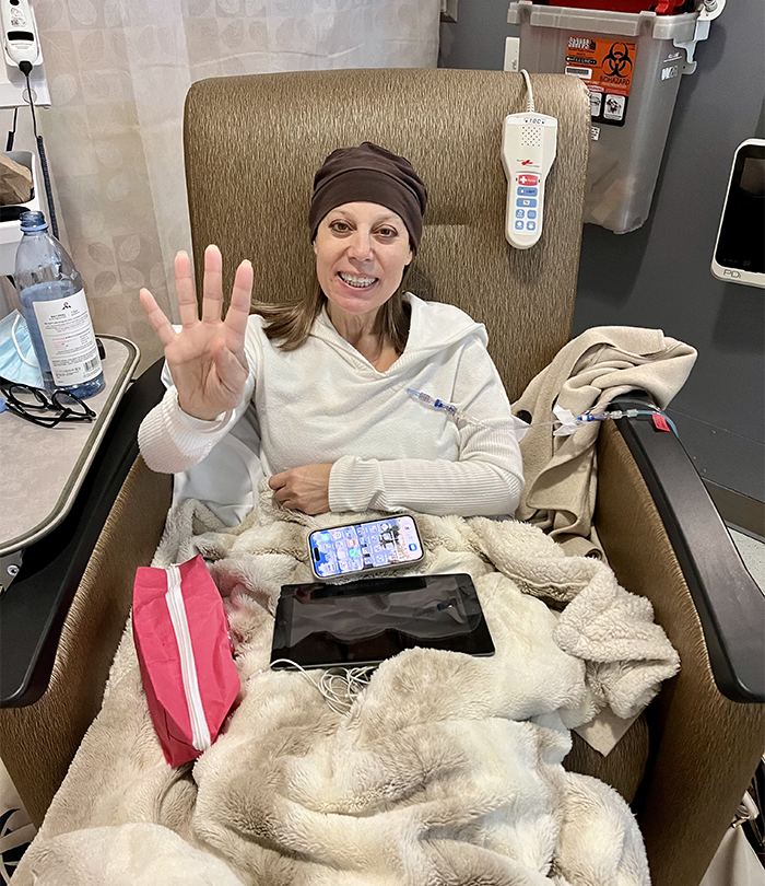 Woman seated and signaling four with her hand to indicate her fourth round of chemotherapy.