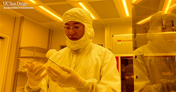 A researcher in a clean room gown works on a device