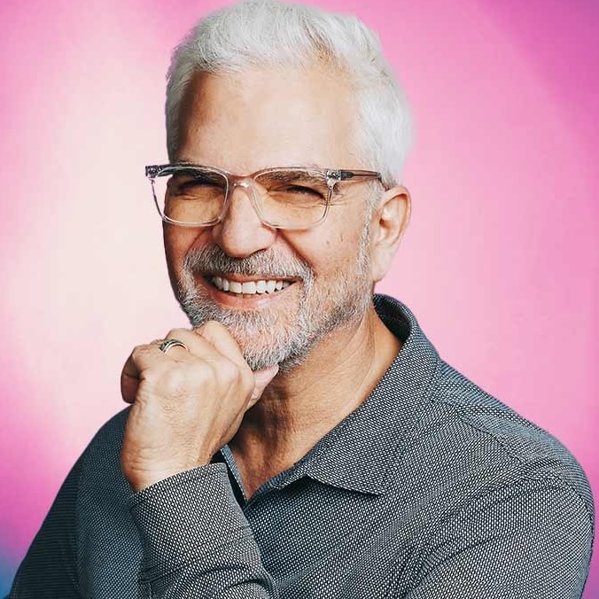 Photo of man with gray hair and glasses smiling with hand to chin
