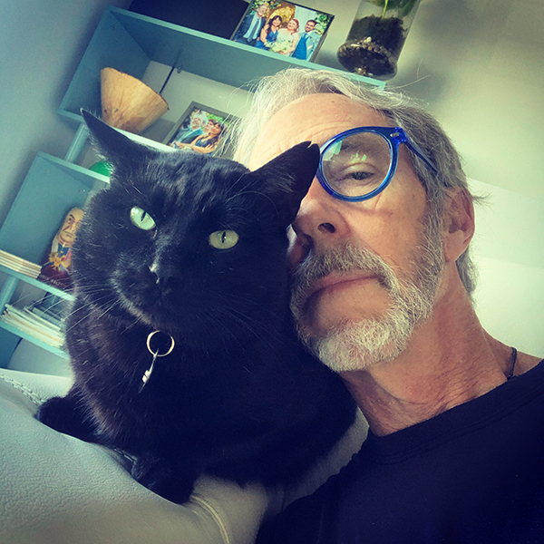 Portrait of Randy Hampton in blue glasses peeking from behind black cat