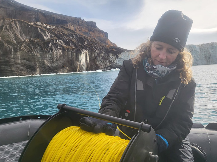 A woman operates a remotely operated vehicle in front of a small glacier in the Antarctic Peninsula.