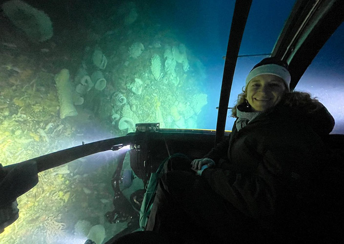 A woman in a submersible looks out the window during an underwater dive