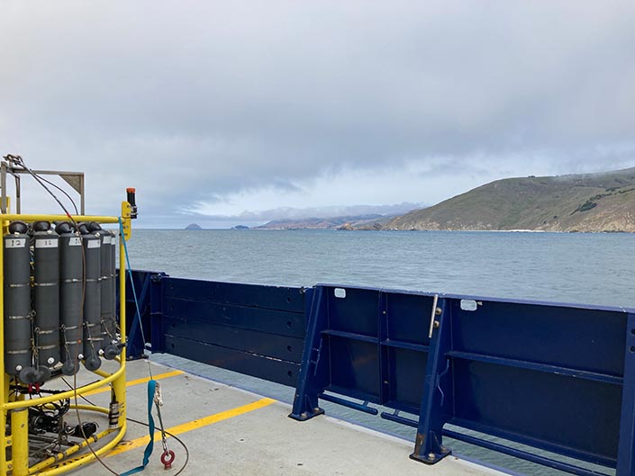 A CTD on a ship, with the ocean and coatline in the background.