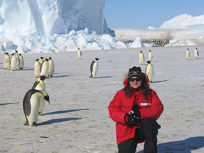 A woman in the field in Antarctica, surrounded by penguins.
