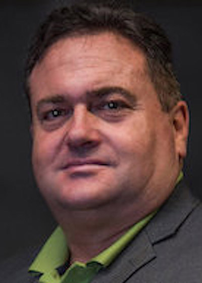 Portrait of a man in a green collared shirt and gray blazer against a dark gray background.
