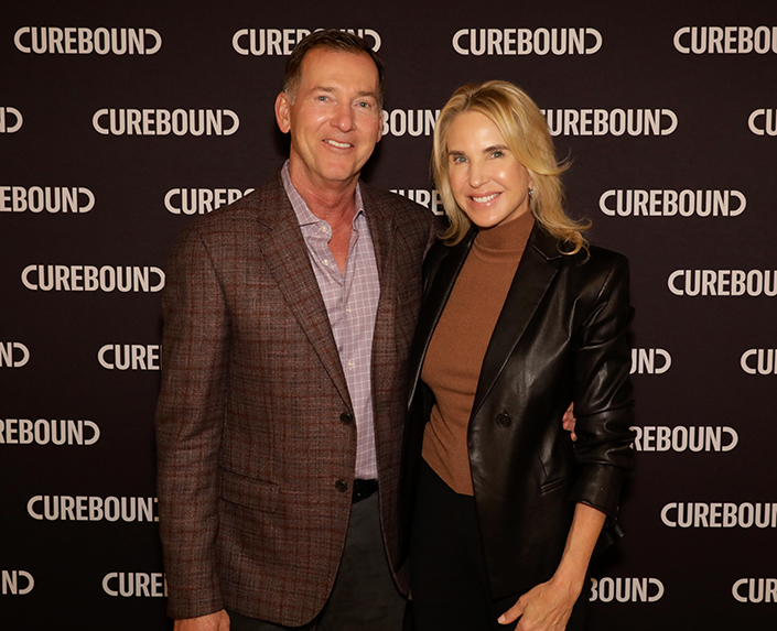 Photo of man and woman smiling in front of Curebound step and repeat