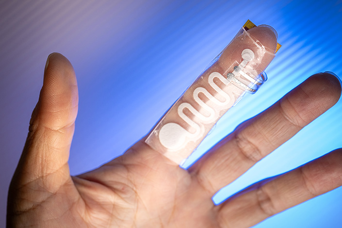 Palm side of a person's hand with the index finger wearing a clear plastic strip that is covered by a white, squiggly line.