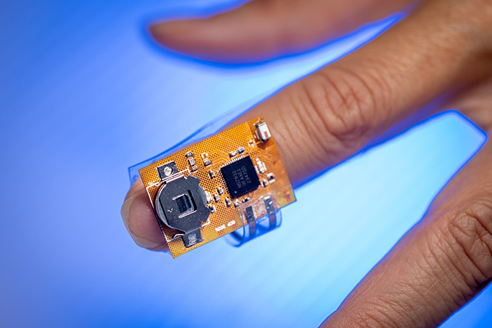 Small, yellow circuit board worn on the nail of a person's index finger.