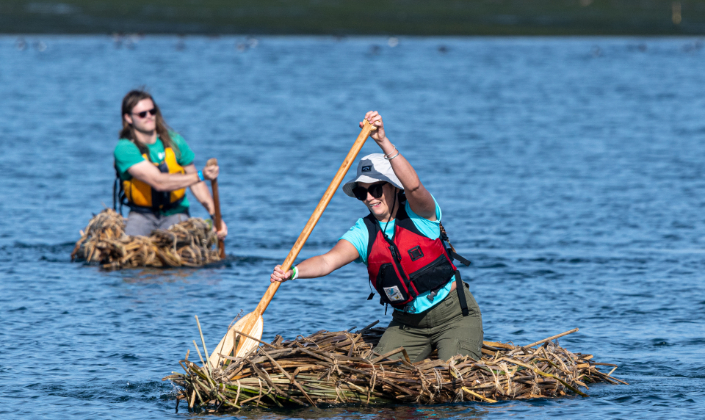 Two people use paddles to maneuver tule boats.