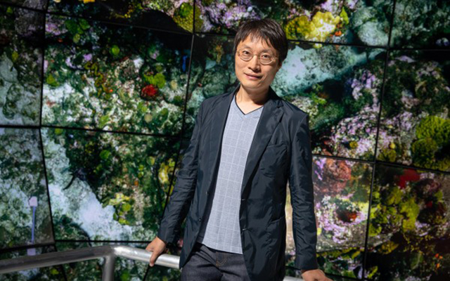 Portrait of the composer standing in front of a display showing images from his Hearing Seascapes audiovisual work.