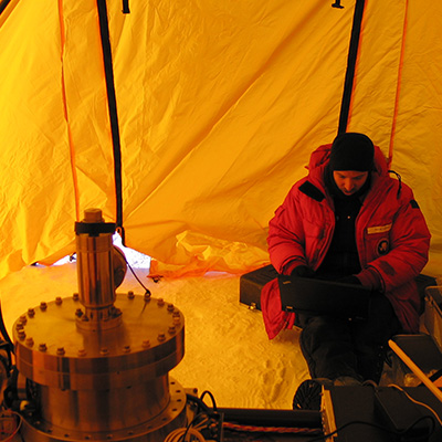 Lesser sits in a yellow-lit tent in his red jacket, taking notes.
