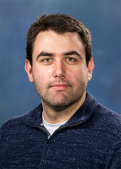 Portrait of a man wearing a dark blue sweater against a blue background.