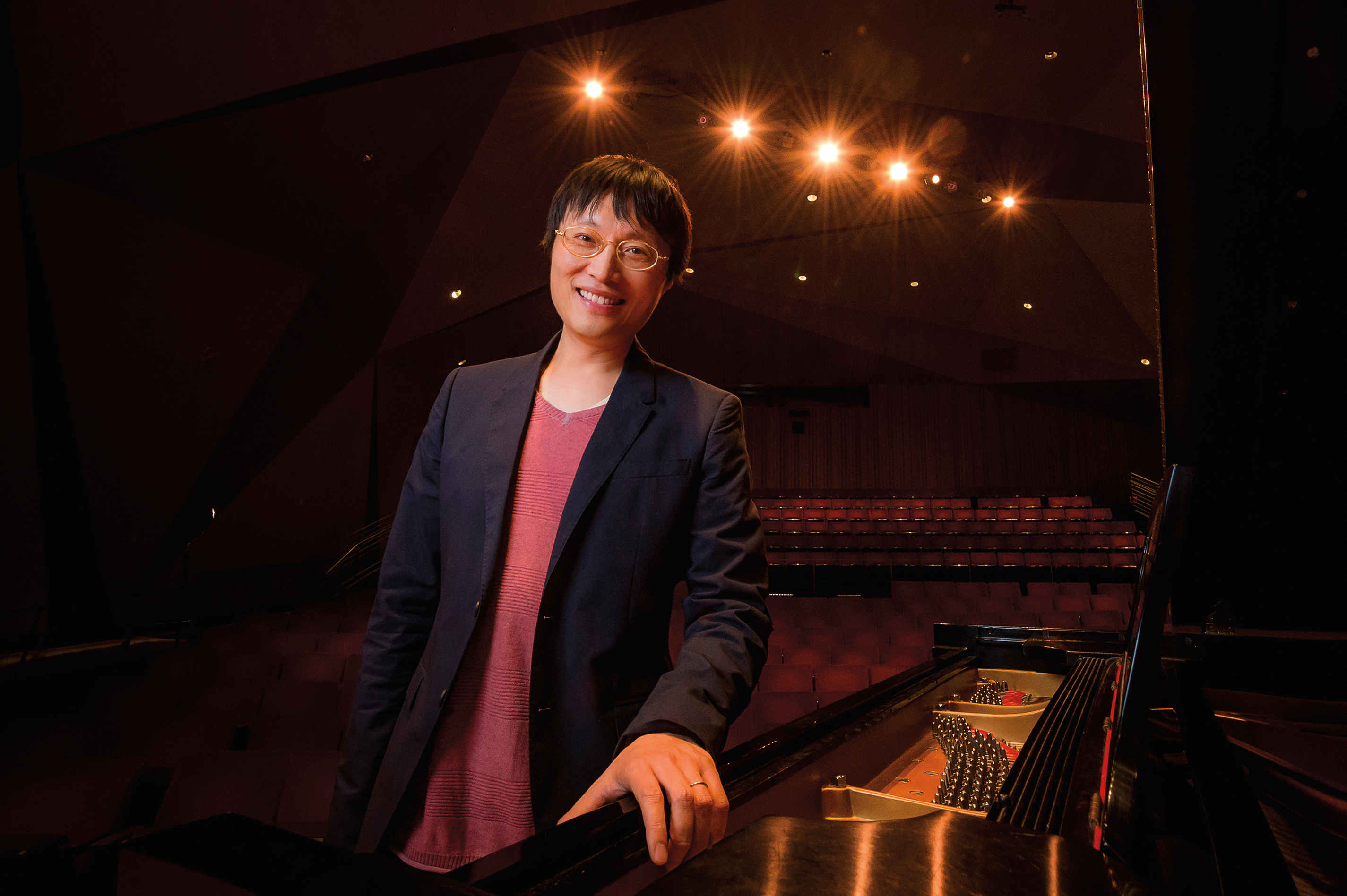 Lei Liang standing on stage with his hand on a piano.