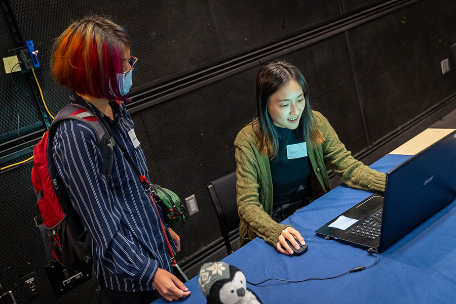 Intern Andrea Kang with the Qualcomm Institute's NeuroDiversity in Tech internship watches a visitor play a game.