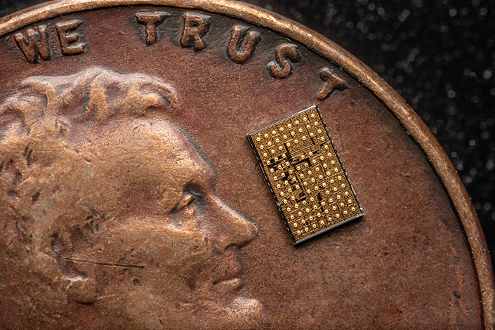 A small, rectangular golden circuit sitting on a U.S. penny.