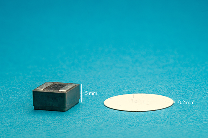 A thin, round white disk next to a thick, gray block against a blue-green background.
