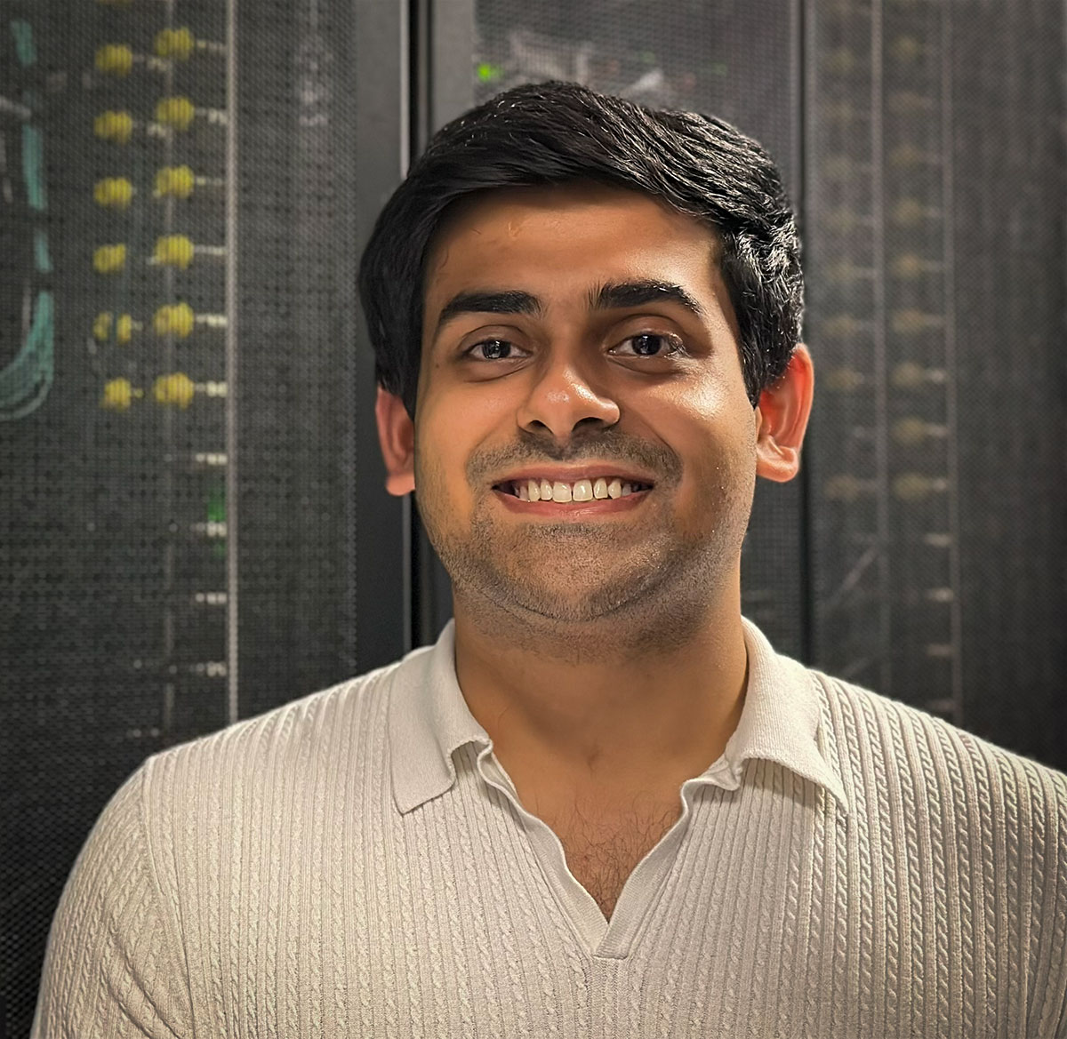 Headshot of Gaurav Guru in front of supercomputer racks. 