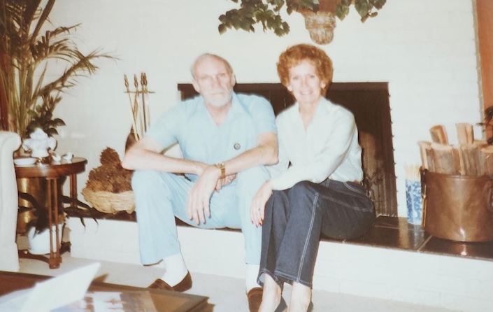 Photo from the 1980s of a man and woman sitting on a fireplace hearth