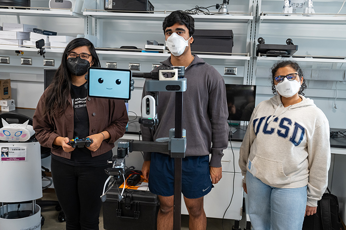 People standing behind a robot with a screen displaying a cartoon face.