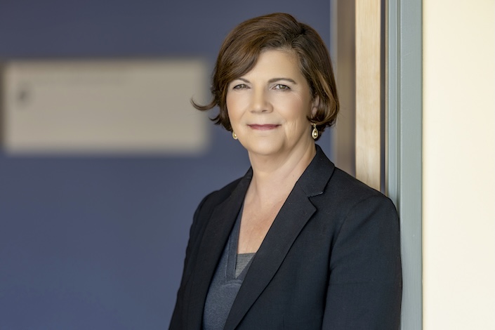 Photo of woman in a jacket against a wall with a slight smile
