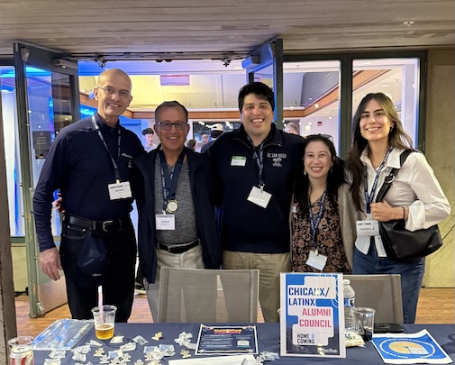 Photo of group of five people in front of a table with a sign that says Chicax/Latinx Alumni Council