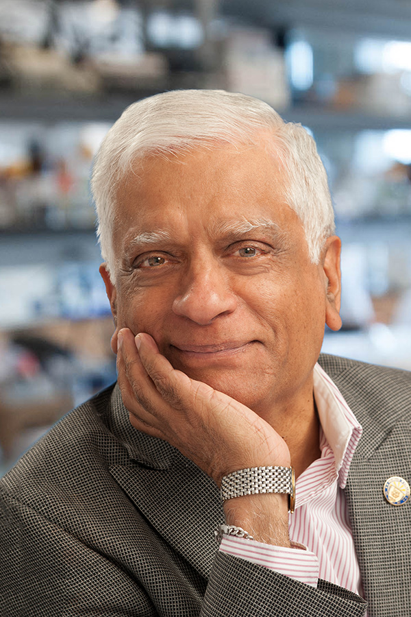 Lab portrait of white-haired Suresh Subramani leaning on one hand