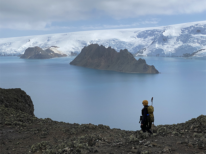A woman hiking in the Antarctic Peninsula, with a scenic polar backdrop and the ocean in the background.