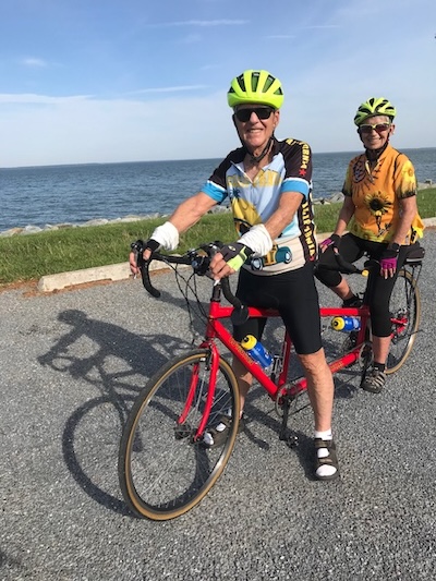 Man and woman on a tandem bike smiling in front of the ocean