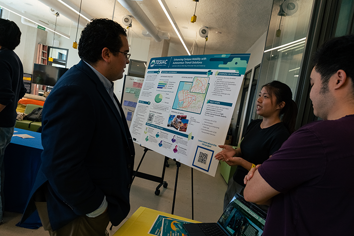 i4X student team chats with attendee about their novel, mobile transit planning solution.